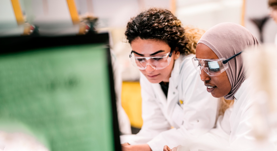 To kvindelige studerende fra Science i hvide kitler med beskyttelsesbriller